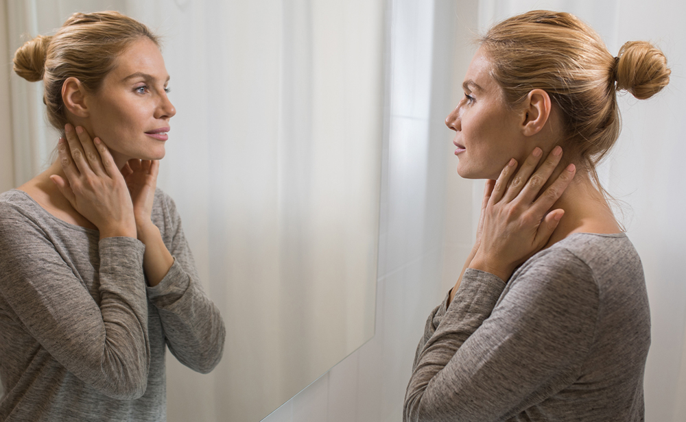Young beautiful woman looking herself in the mirror at bathroom. Neck Lift in Phoenix, AZ